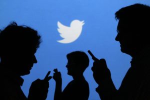 People holding mobile phones are silhouetted against a backdrop projected with the Twitter logo in Warsaw