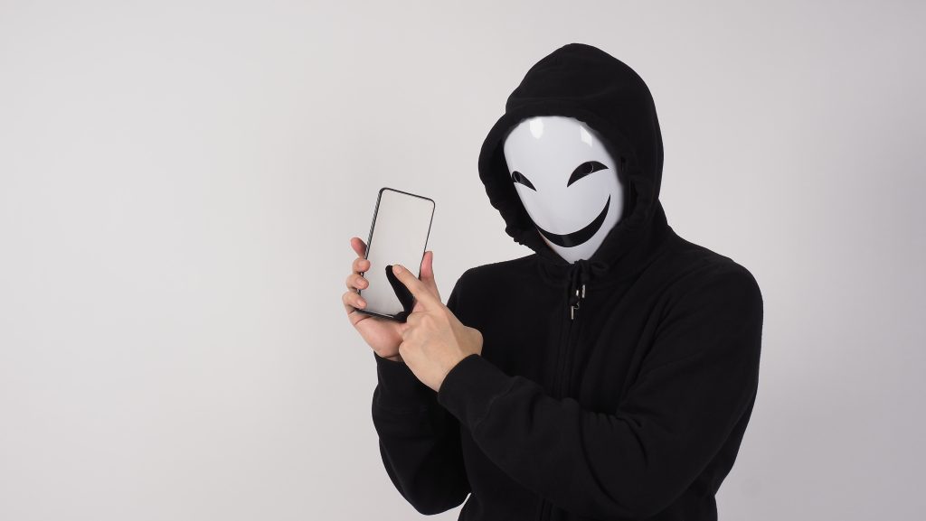 sicurezza-Anonymous hacker and face mask with smartphone in hand-identità digitali